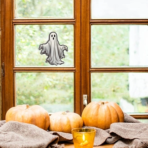 Ghost window sticker applied on glass with Halloween pumpkins and candles background