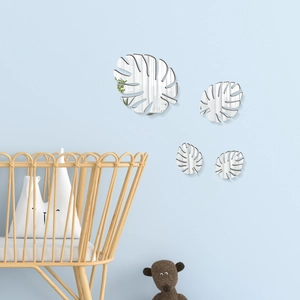 Close-up of four silver monstera leaf mirror wall stickers in a cozy blue nursery setting