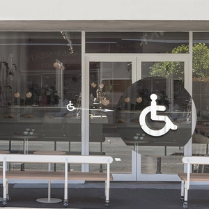 Close-up of a white 3D handicap wheelchair icon sticker applied on a glass door
