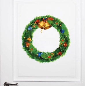 Close-up of a Christmas wreath with gold bells, red bow and colorful ornaments on white door