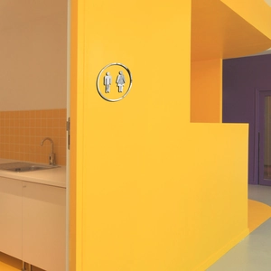 Macro detail of round silver acrylic restroom sign on a vibrant yellow wall