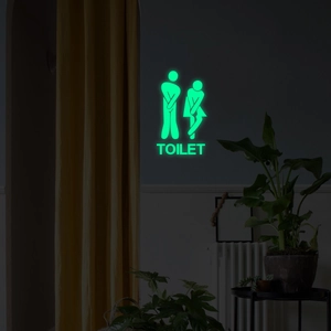 Leuchtend grüner Toiletten-Aufkleber mit humorvollen Figuren in schwachem Licht gezeigt