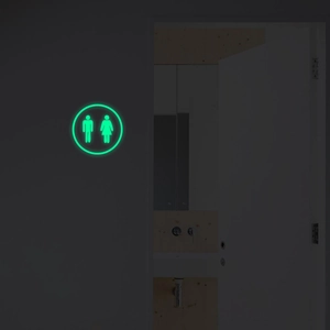 Glow-in-the-dark circular restroom sign with green fluorescent male and female symbols