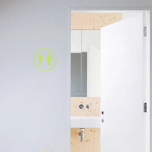 Glow-in-the-dark bathroom door sign with minimalist male and female icons on a white wall