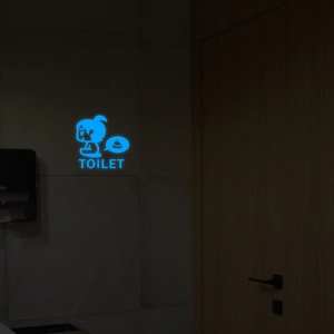 Detail eines leuchtenden blauen Toilettenschilds mit Cartoon-Mädchen im Dunkeln