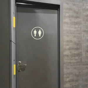 Luminous round bathroom door sign with glowing male and female silhouettes on a dark grey door