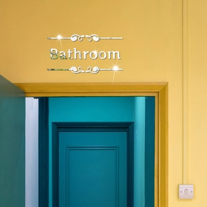 Detail of silver acrylic mirror bathroom sign with decorative scroll lines on a wall