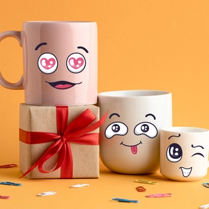 Ceramic mugs set with cute cartoon faces on gift box with festive orange background