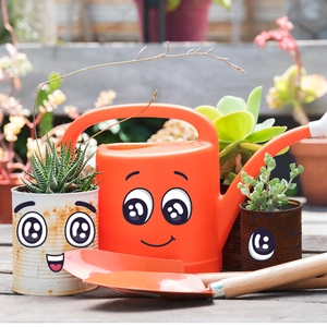 Detail of garden tool set with funny smiley face stickers on orange watering can and pots
