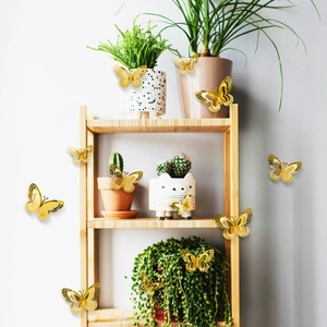 3D metallic gold hollow butterfly wall stickers displayed on wooden shelf and green plants