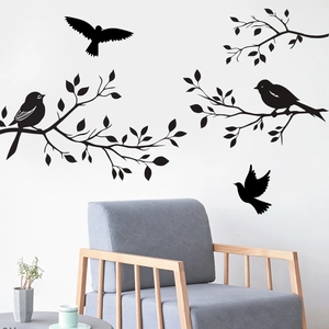 Modern black wall decal with branches and birds on white wall over a grey chair