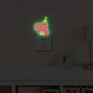 Luminous dinosaur wall sticker glowing green around a power socket in a dark bedroom