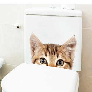 Detail view of a 3D cartoon ginger cat wall sticker applied on a white bathroom toilet surface