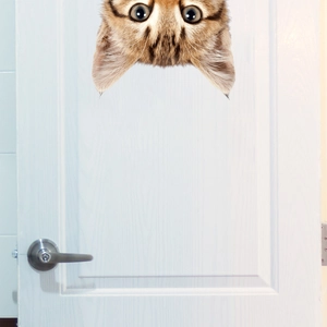 Close-up of 3D orange tabby cat door sticker peeking from the top of a white wooden door