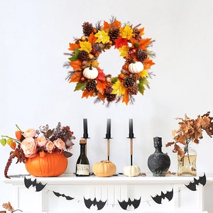 Detail of autumn wreath with maple leaves, pine cones, and white pumpkins on a white wall