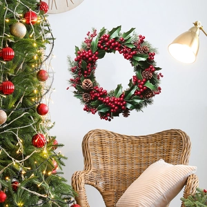 Christmas wreath with red berries and pine cones hanging on white wall with festive decor