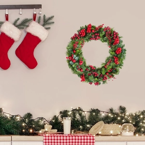 Détail d'une couronne de Noël avec baies rouges et aiguilles de pin sur un mur clair