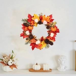 Couronne d'automne avec feuilles d'érable, citrouilles et pommes de pin sur mur blanc