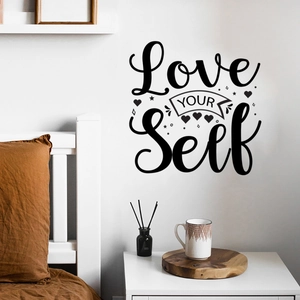 Detail view of black Love Yourself wall decal on a white wall in a cozy bedroom scene