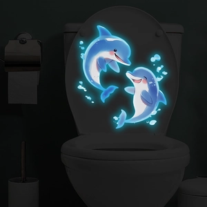 Gros plan d'autocollants dauphins lumineux bleus sur un couvercle de WC dans le noir