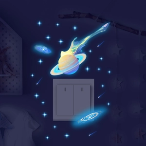 Luminous blue Saturn and galaxy wall stickers glowing around a wall switch in a dark room