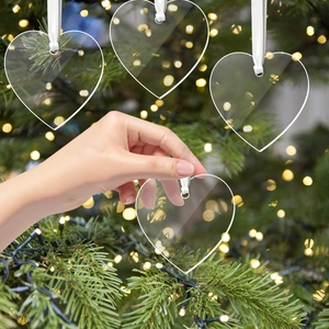 Clear acrylic heart Christmas ornament held by hand with warm holiday lights background