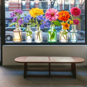 Set of six colorful mini glass vases with vibrant flowers on a bright windowsill