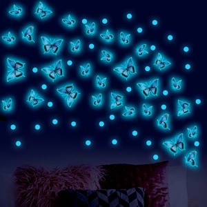 Luminous wall sticker set with glowing blue butterflies and dots on dark bedroom wall
