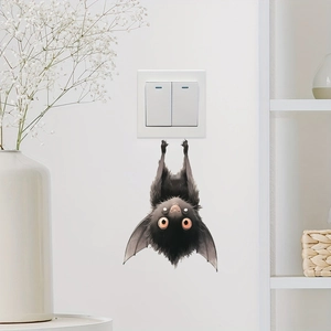 Cartoon black bat wall sticker with orange eyes hanging on a white wall above a switch