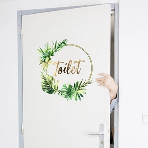 Detail of green tropical leaves and golden Toilet text sticker on a white door