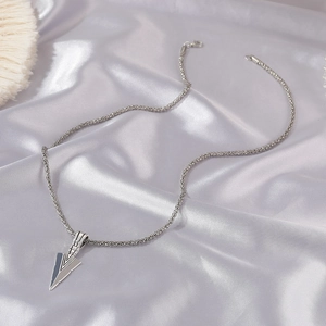 Detailed view of silver arrow pendant with wheat chain on elegant silk fabric background