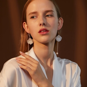 Detail of long gold earrings with white petals, pearls, and a ballet dancer silhouette