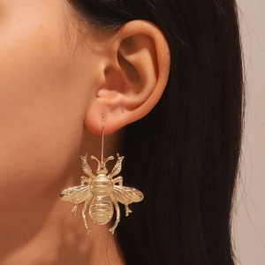 Close-up of golden bee-shaped dangle earrings with intricate wing texture on a model
