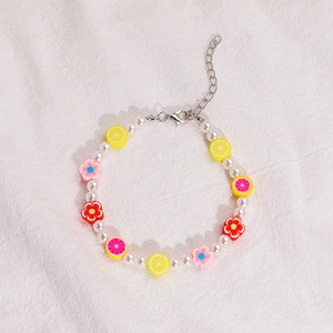 Detalle de pulsera con perlas sintéticas y colgantes de flores en arcilla polimérica