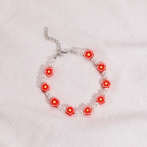 Detalle de pulsera de cuentas con perlas blancas, flores de arcilla roja y cierre plata