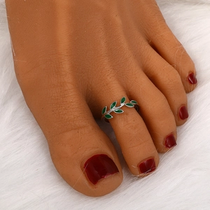 Detailed view of silver plant-shaped toe ring with green enamel leaves on white fur