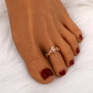 Detail view of a rose gold twig-shaped toe ring on a model with red nail polish