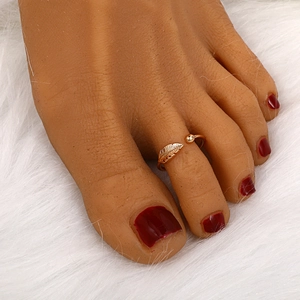 Detailed close-up of a golden leaf toe ring with a minimalist bead on a soft white background