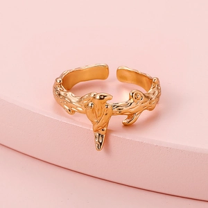 Macro detail of a vintage golden bird and branch open ring on a pink stone background
