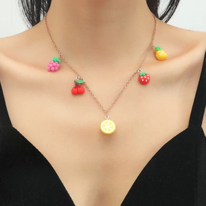 Dettaglio della collana dorata con cinque ciondoli a forma di frutta colorata su modella