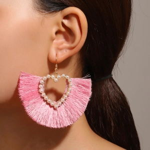 Detailed view of pink fan-shaped fringe earrings with heart pearl accents on a model