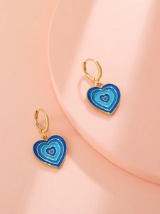Detail of blue heart dangle earrings with gold hoop closure on pink background