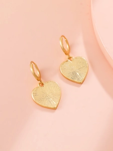 Close-up of golden heart drop earrings with radiant sunburst texture on pink background