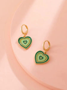 Detail of golden hoop earrings featuring green enamel heart pendants with gradient circles