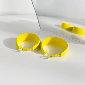 Macro shot of large bright yellow matte hoop earrings with a mirror reflection on white