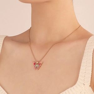 Primo piano di una collana con ciondolo a farfalla in smalto rosso e blu su catena dorata