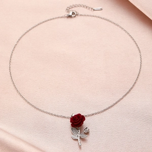 Detail view of the silver chain necklace with red rose pendant on pink satin background