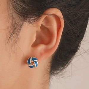 Close-up of a blue enamel knot stud earring worn by a model to show texture and size