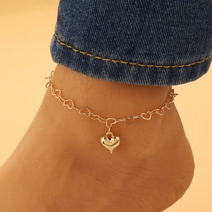 Dettaglio di una cavigliera boho dorata con ciondolo a cuore 3D su una catena sottile