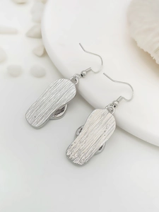 Silver flip-flop drop earrings with brushed texture detail on a beach-themed setup
